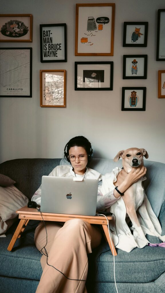 Woman wearing headphones on a video call at her laptop with a dog beside her