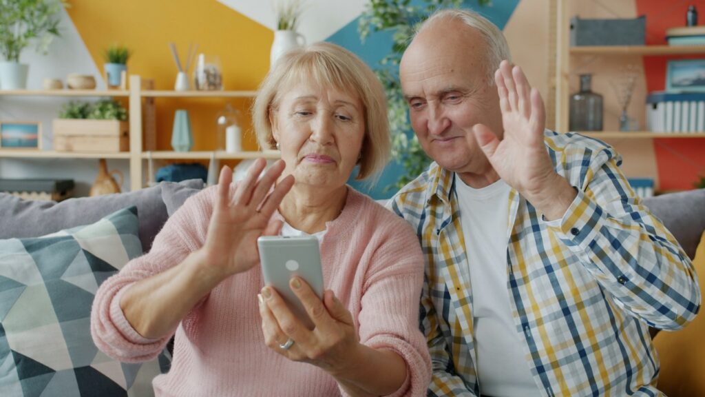 Older couple waving at a smartphone during a video call with family